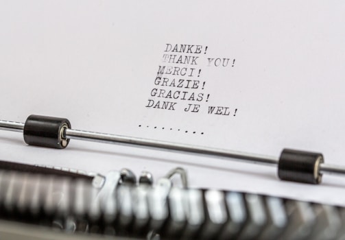 A close-up of a typewriter with a sheet of paper in it. The paper contains the word 'thank you' typed in multiple languages, including German, English, French, Italian, Spanish, and Dutch.