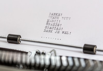 A close-up of a typewriter with a sheet of paper in it. The paper contains the word 'thank you' typed in multiple languages, including German, English, French, Italian, Spanish, and Dutch.