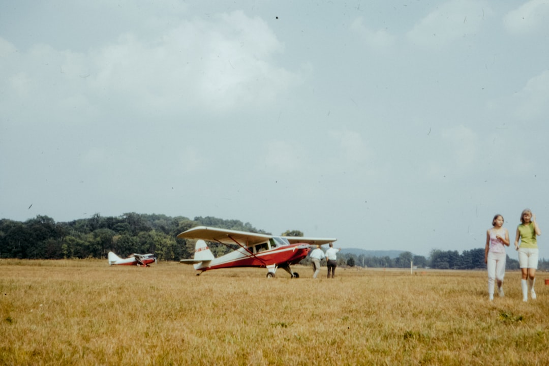 white and red plane on green grass field under white clouds during daytime