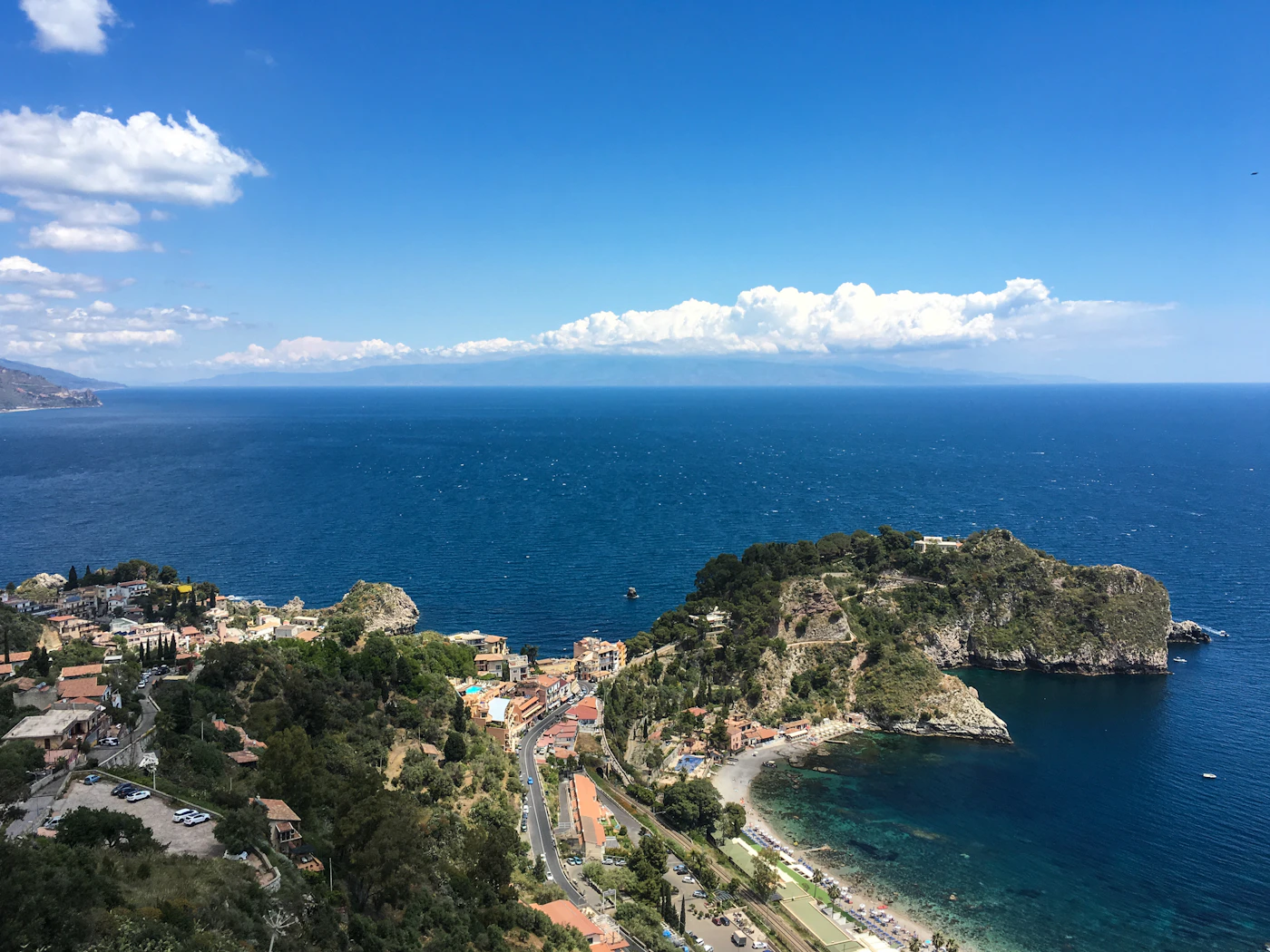 Aerial view of Taormina Sicily showing the ancient Greek theatre perched on the hillside above the town with the turquoise Ionian Sea and coastline stretching below