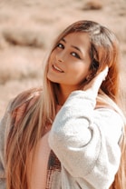 A person with long hair wearing a cozy, textured jacket stands in a natural outdoor setting, exuding a relaxed and content demeanor.