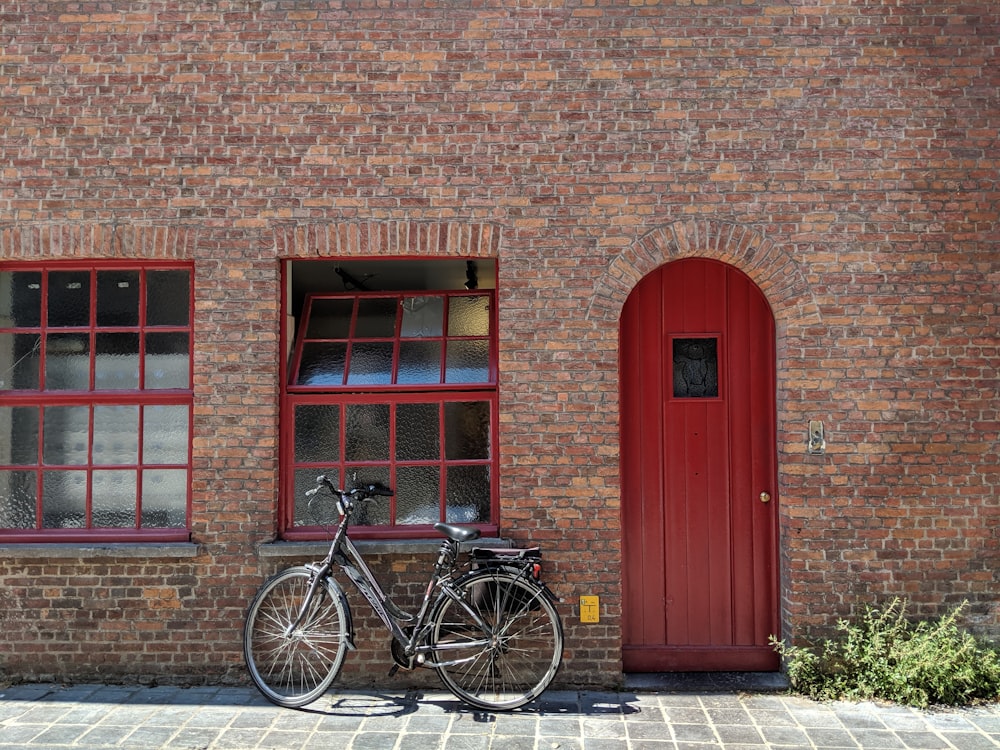 black bicycle parked beside red wooden door