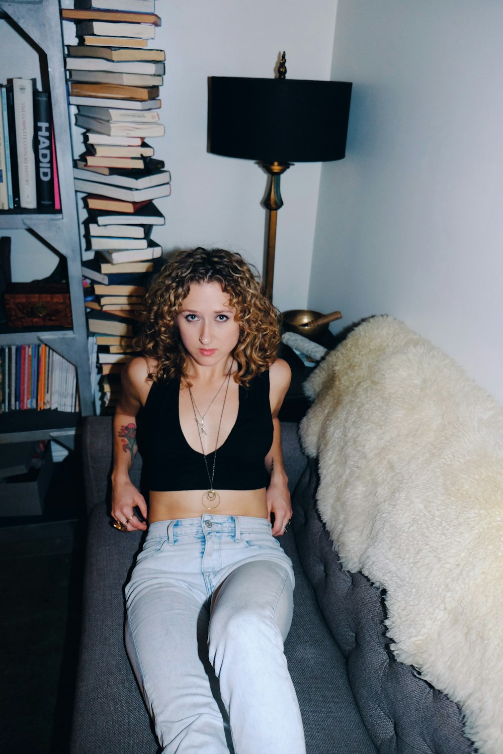 woman in black tank top and blue denim jeans sitting on white fur textile