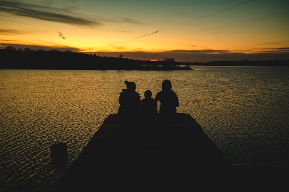 silhouette of 2 people sitting on dock during sunset