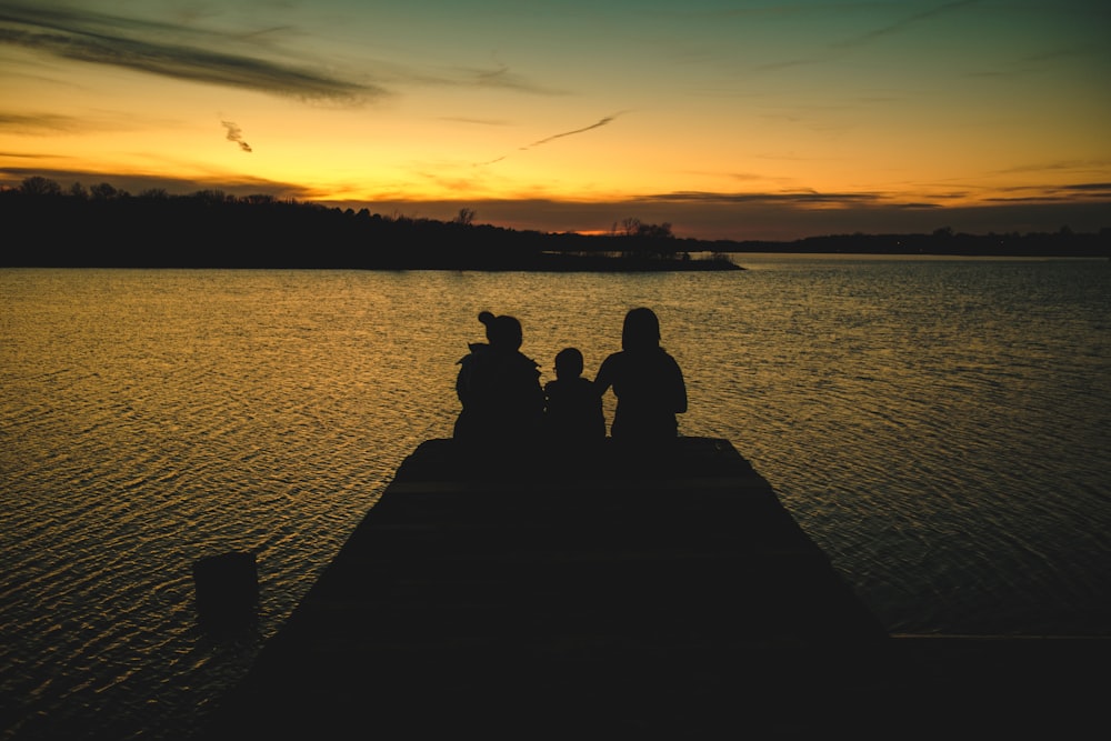 silhouette di 2 persone sedute sul molo durante il tramonto