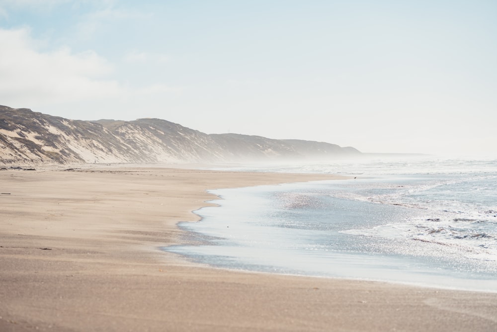 praia de areia marrom com montanha à distância