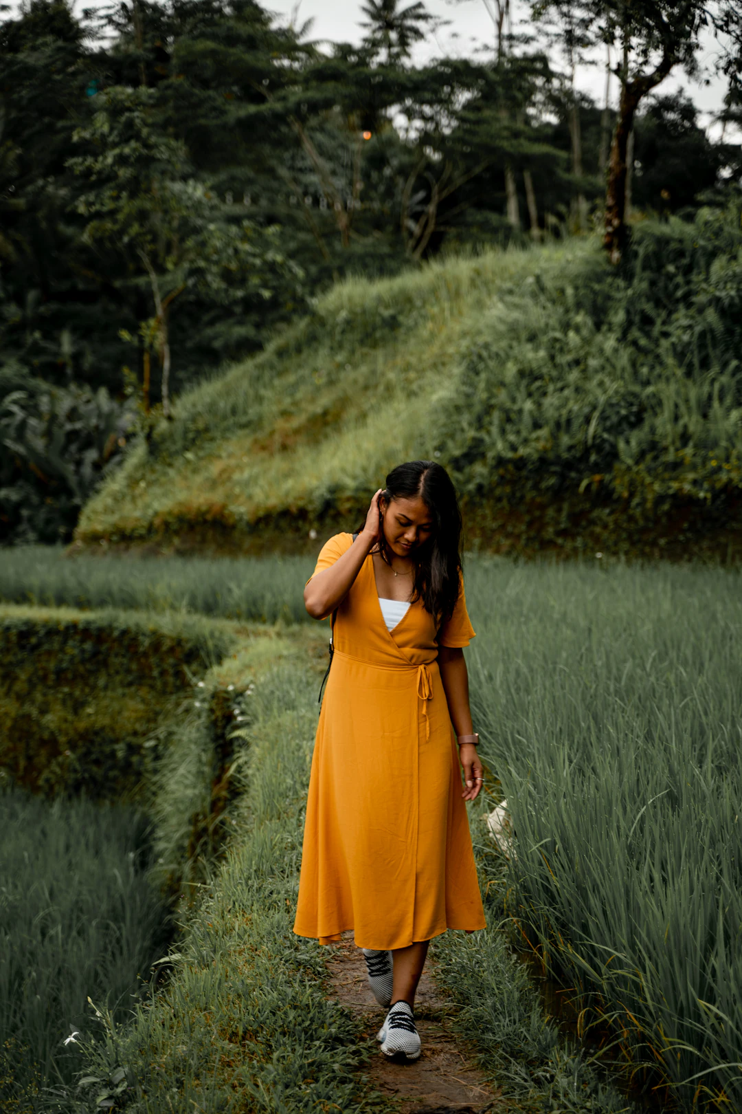 A woman in an orange dress walking along a path through green rice terraces