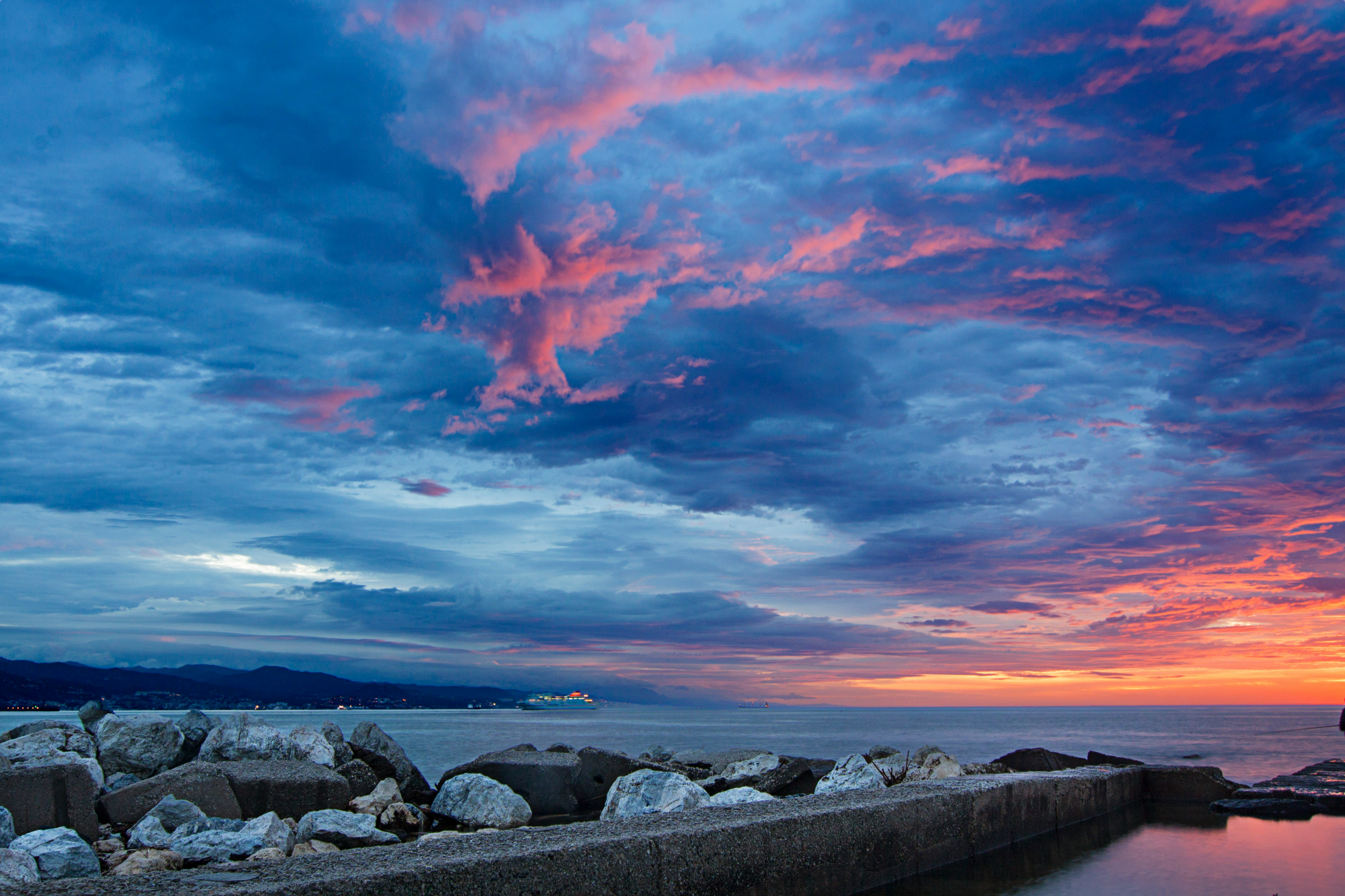 gray rocks on sea shore under orange and blue cloudy sky