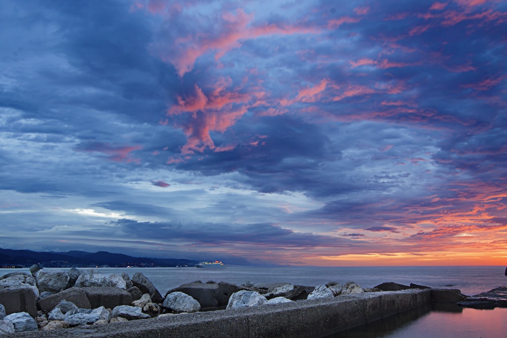 gray rocks on sea shore under orange and blue cloudy sky