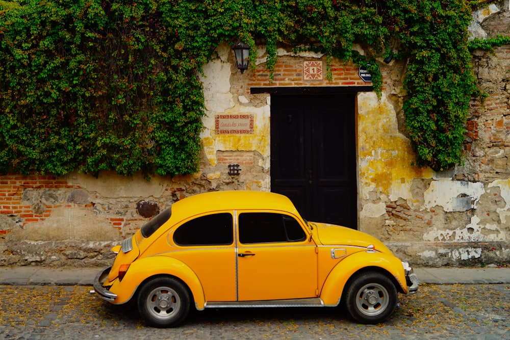 yellow volkswagen beetle parked beside brown brick wall