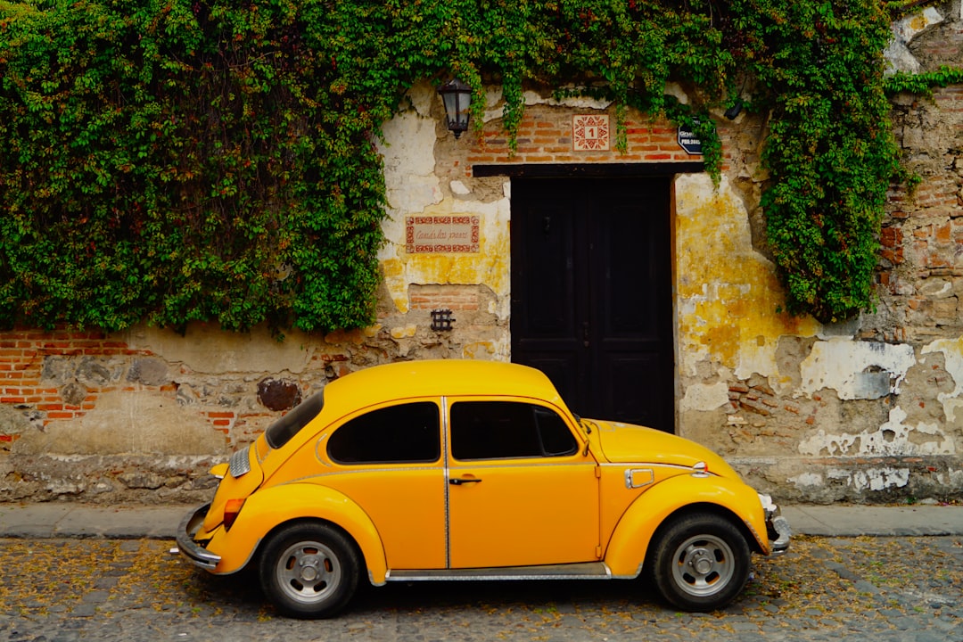 yellow volkswagen beetle parked beside brown brick wall,