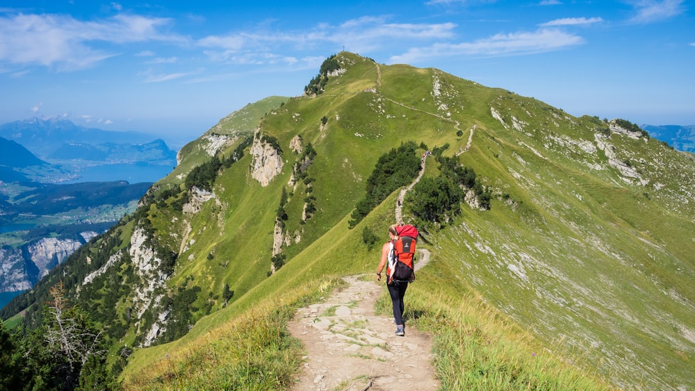 personne en veste rouge marchant sur un champ d’herbe verte pendant la journée