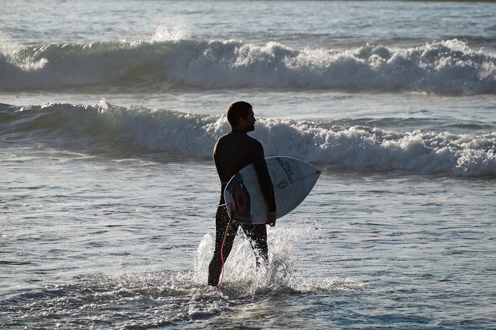 uomo in camicia nera che tiene la tavola da surf bianca sulle onde del mare durante il giorno