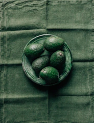 Close-up of ripe Haas avocados arranged on a deep navy cloth with rich gold accents.