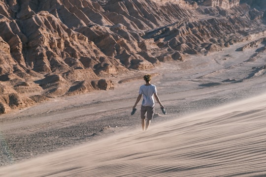 man in white t-shirt and black shorts walking on brown sand during daytime in San Pedro de Atacama Chile