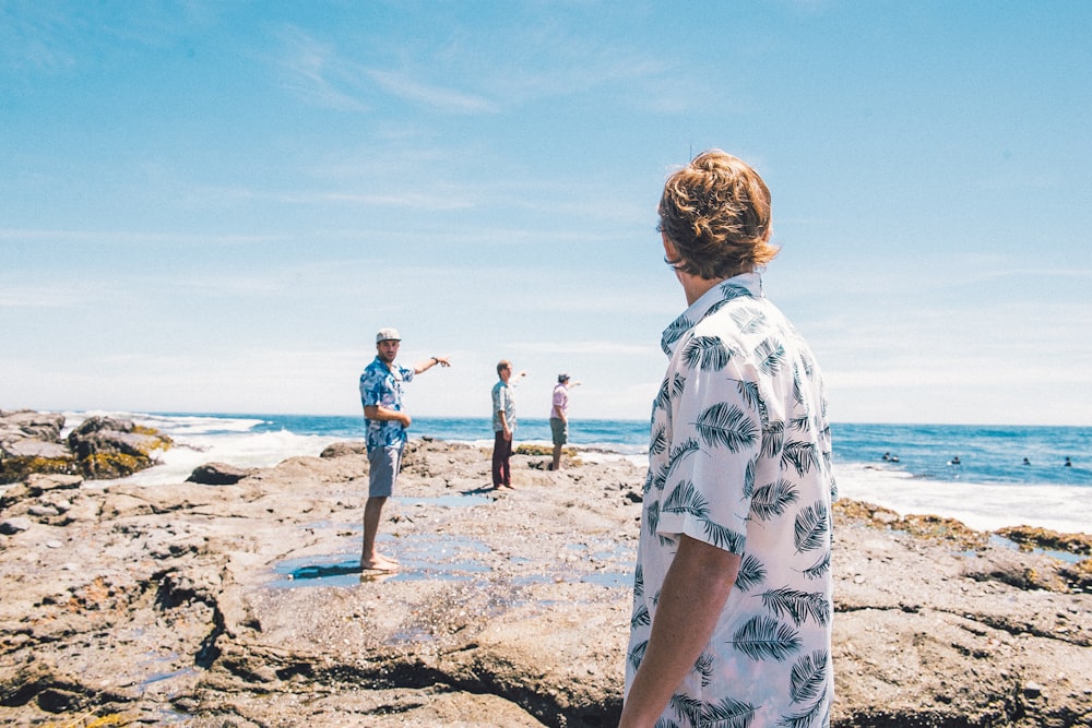 man in white and black floral shirt standing on beach during daytime