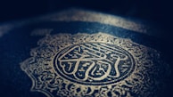 Intricate Arabic calligraphy and ornate patterns are embossed in gold on a dark background, creating a sense of elegance and reverence.