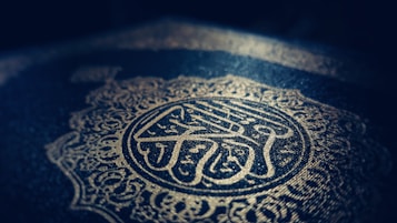 Intricate Arabic calligraphy and ornate patterns are embossed in gold on a dark background, creating a sense of elegance and reverence.