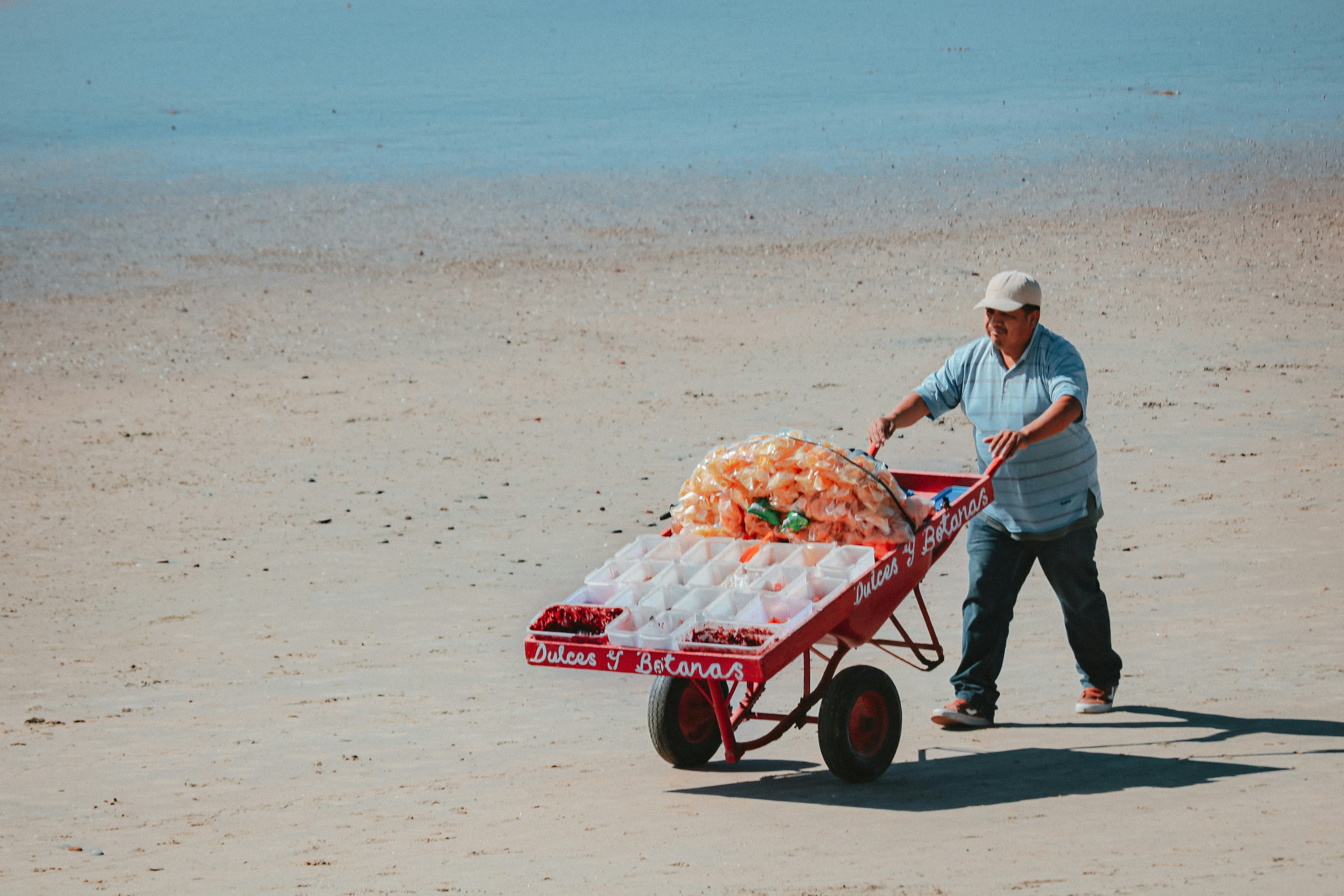 man in white dress shirt and blue denim jeans pushing red and white cart on beach