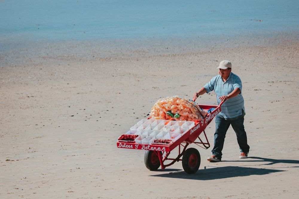 man in white dress shirt and blue denim jeans pushing red and white cart on beach