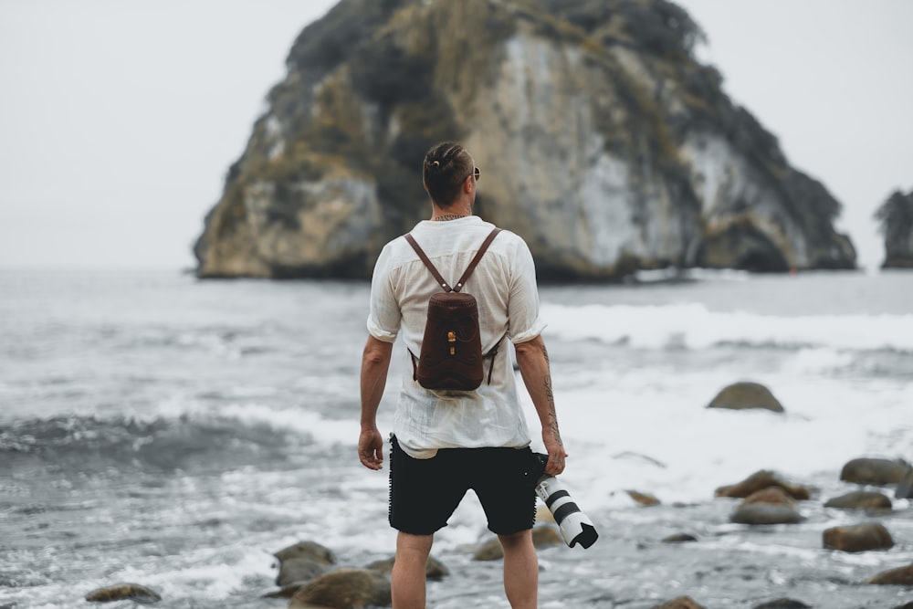 man in white dress shirt and black shorts standing on rock near body of water during