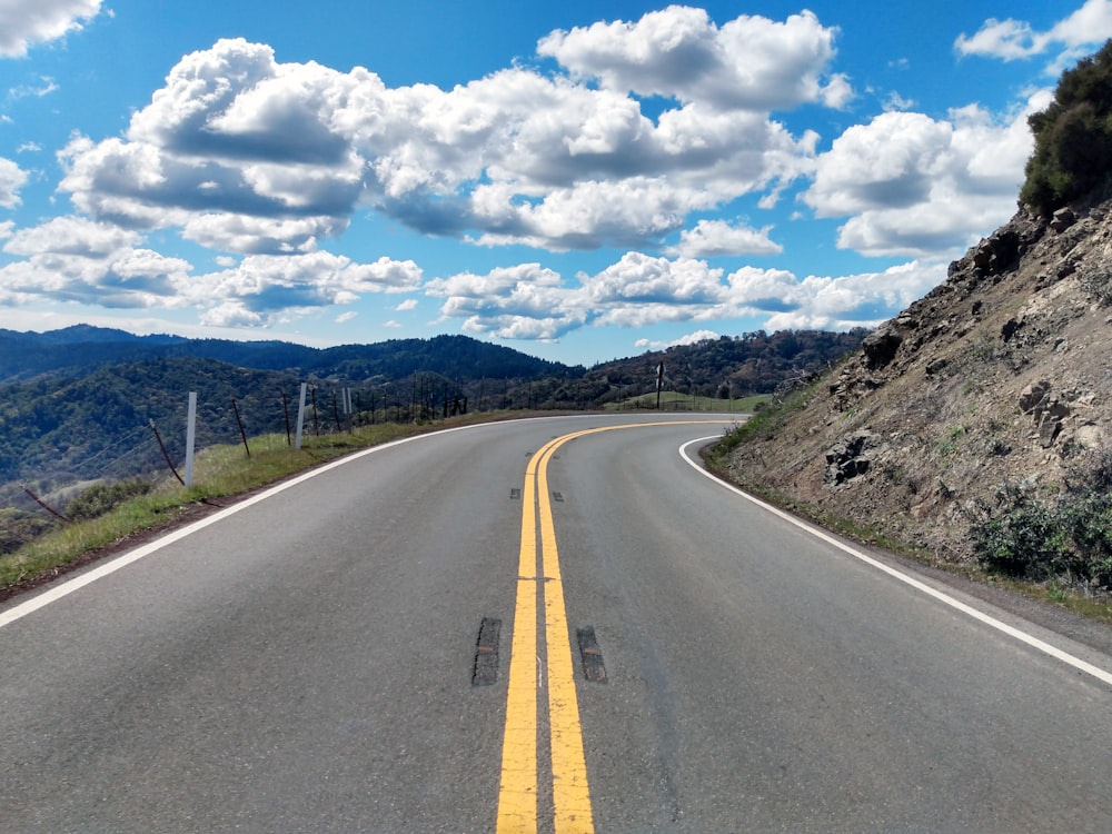 gray concrete road under blue sky and white clouds during daytime