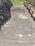 A set of concrete steps leads downward, bordered by a stone retaining wall on one side and a wooden railing on the other. Sparse vegetation grows between the stones, and the steps appear slightly weathered. At the bottom of the steps is an area of grass and greenery.