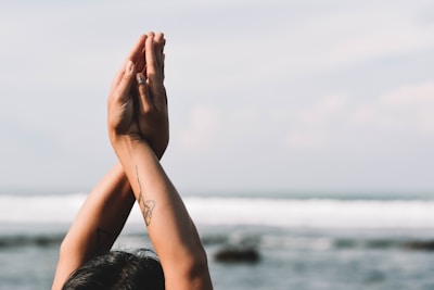 Two hands are positioned in a prayer pose with a blurred ocean background, conveying a sense of calm and reflection.