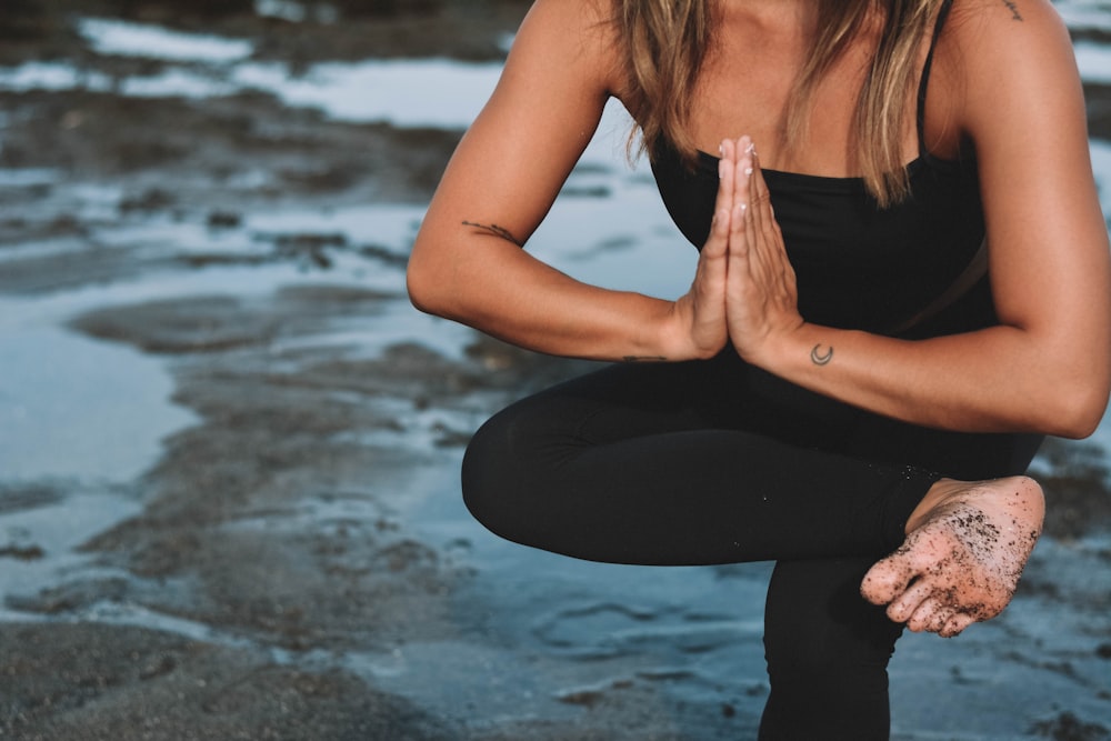 woman in black tank top and black leggings sitting on beach shore during daytime