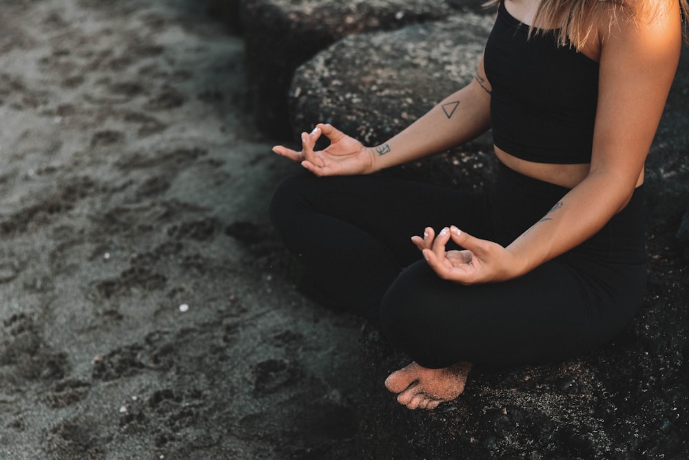 woman in black tank top and black pants sitting on gray rock