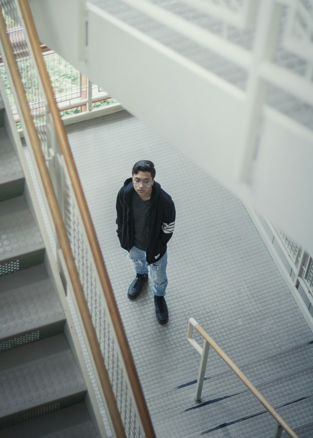 man in black and white adidas jacket and blue denim jeans standing on white staircase