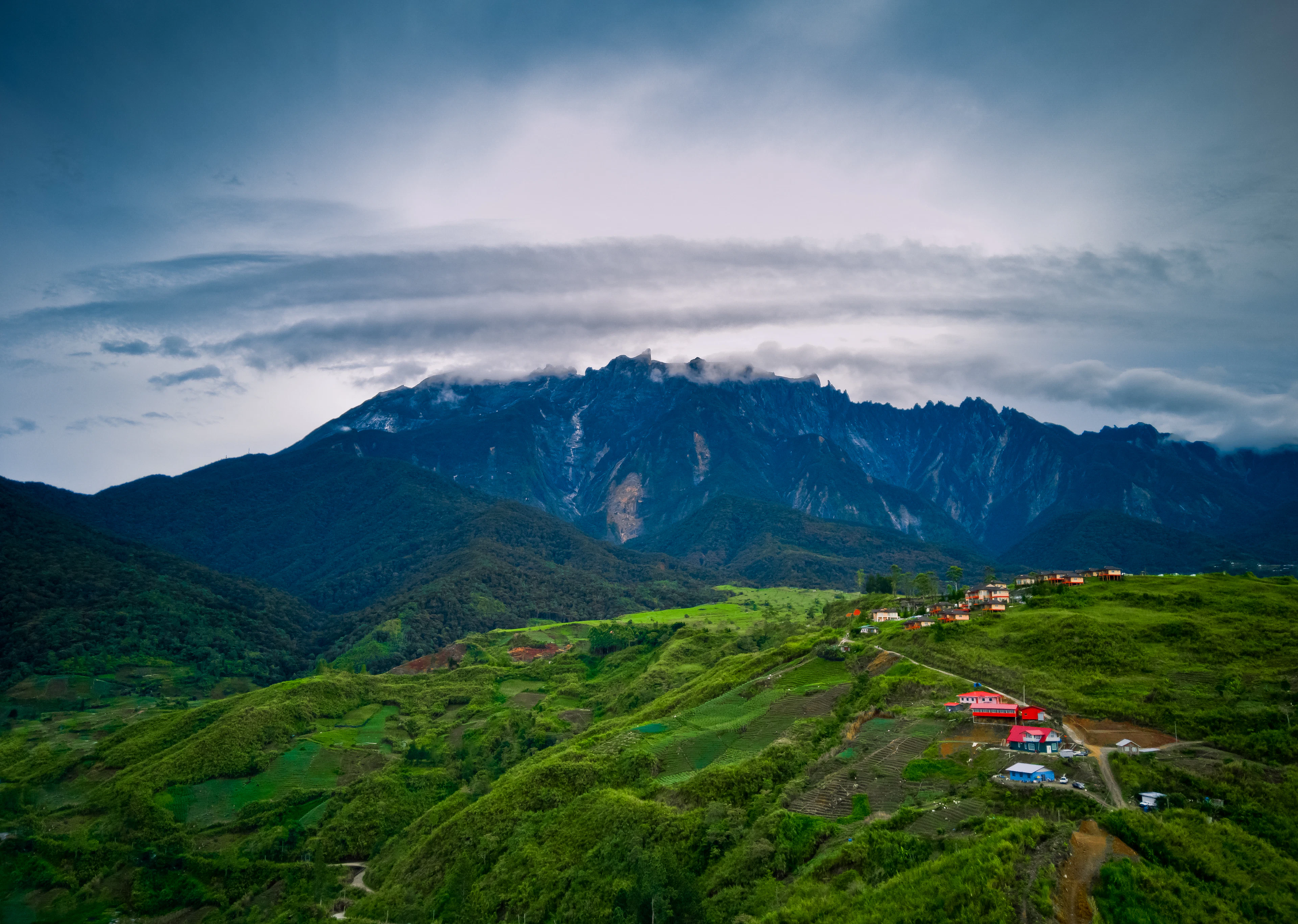 The granite summit ridge of Mount Kinabalu under low cloud, above green hills, Sabah, Borneo