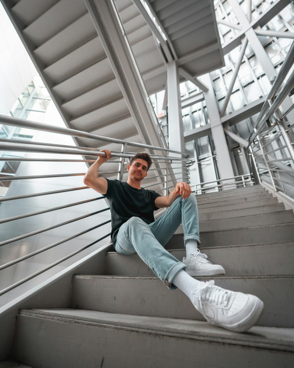 man in blue t-shirt and white pants sitting on brown wooden stairs