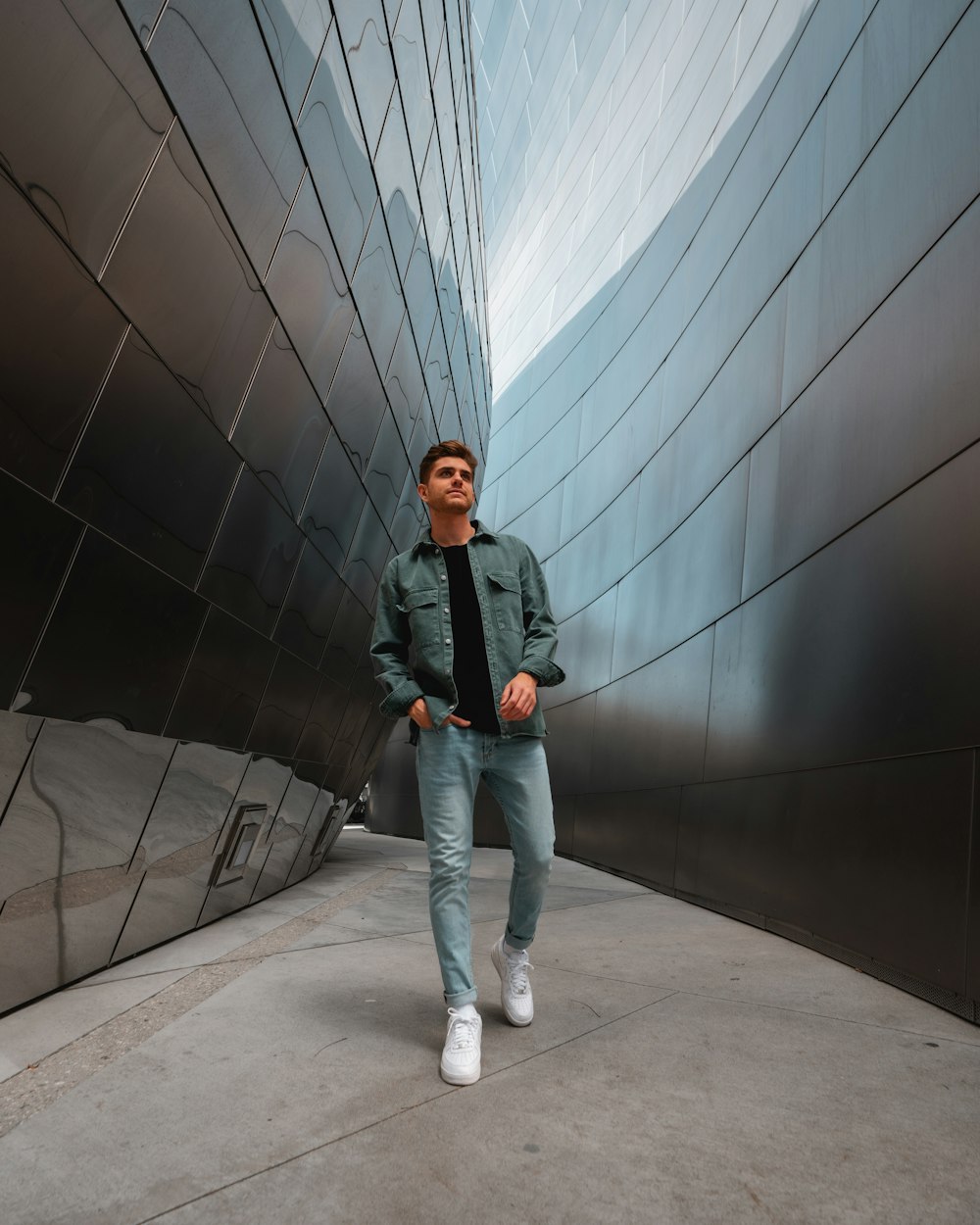 woman in black jacket and blue denim jeans standing beside gray wall