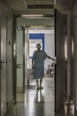 A patient walking with a physical therapist in a bright room.