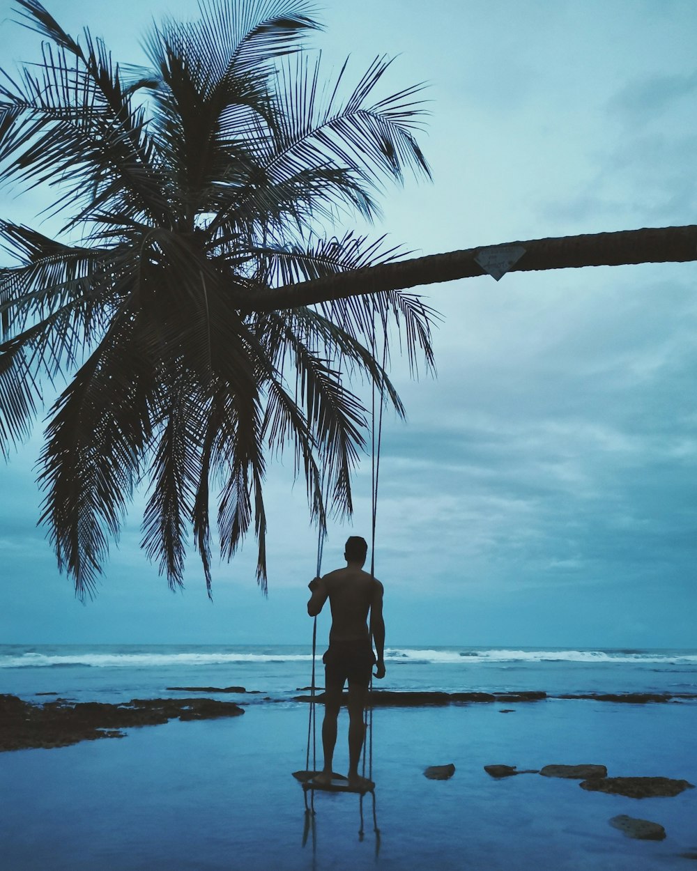 homme en chemise noire et short noir debout sur le rivage de la plage pendant la journée