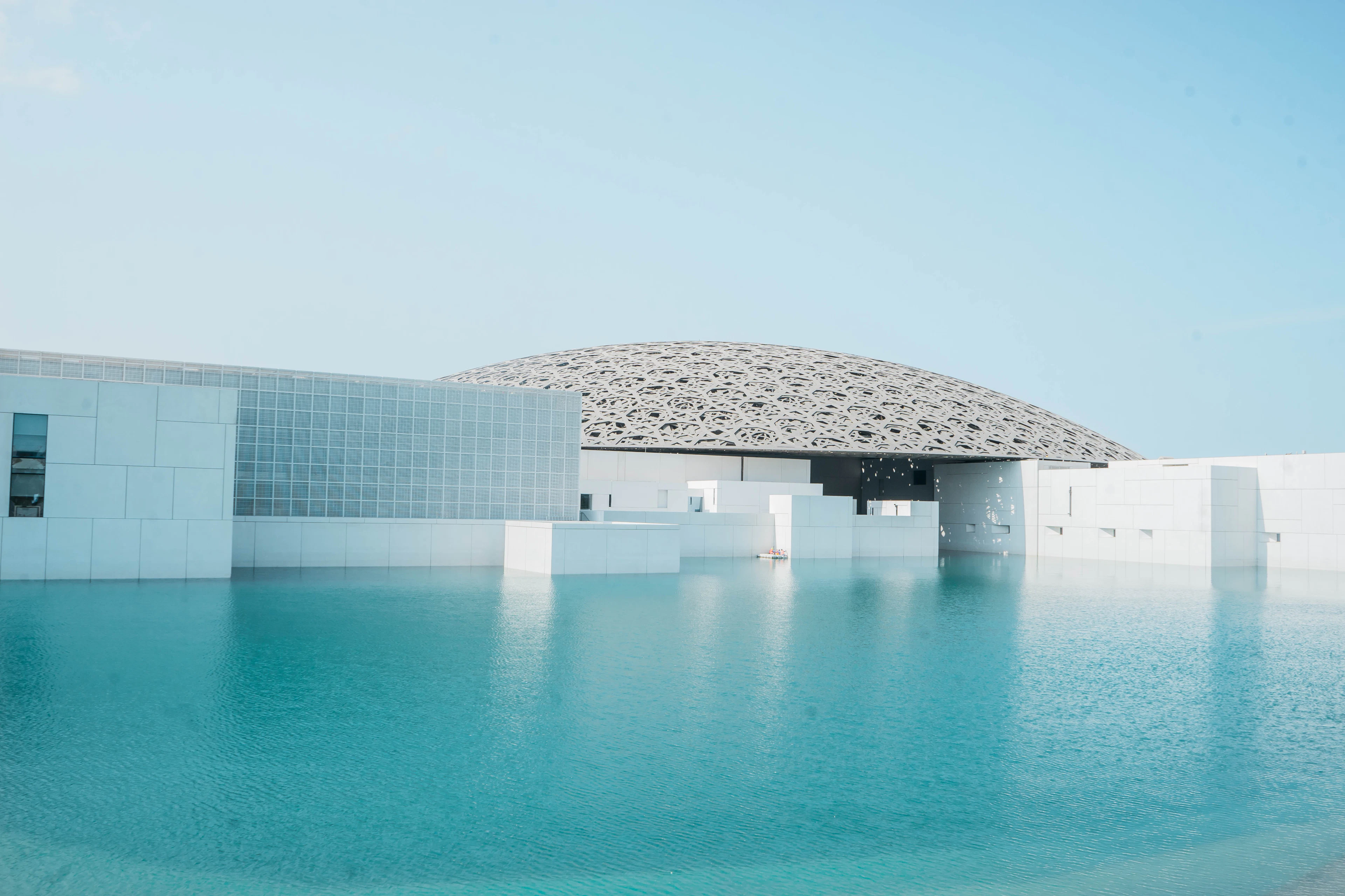 The dome and white pavilions of the Louvre Abu Dhabi above calm water