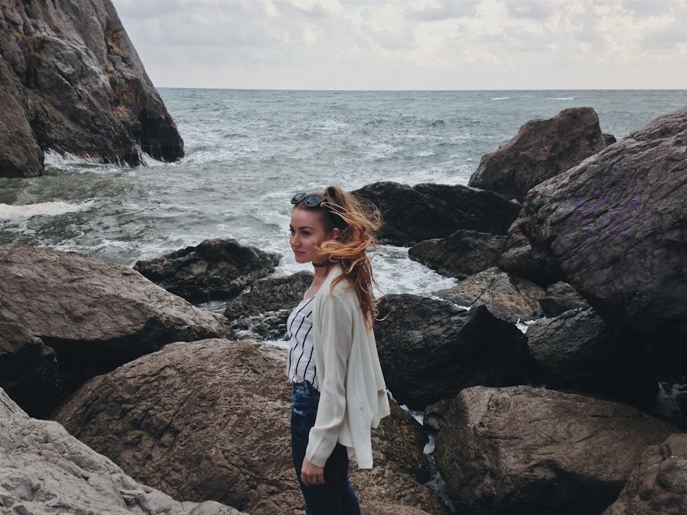 woman in white long sleeve shirt standing on rocky shore during daytime