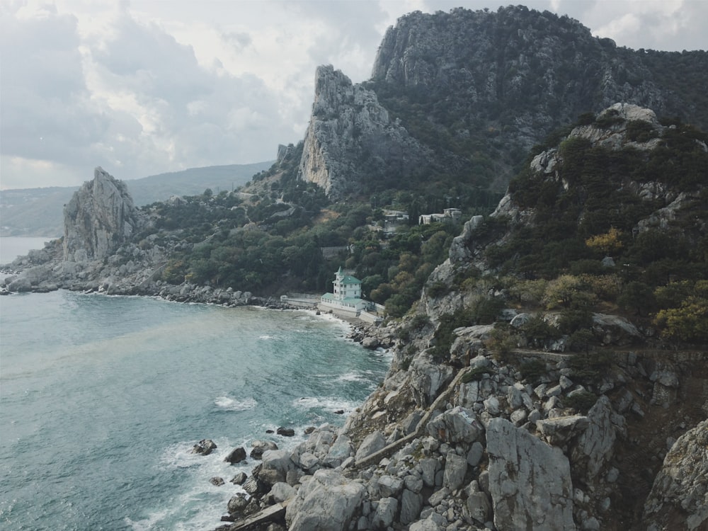 green and brown rocky mountain beside blue sea under white cloudy sky during daytime