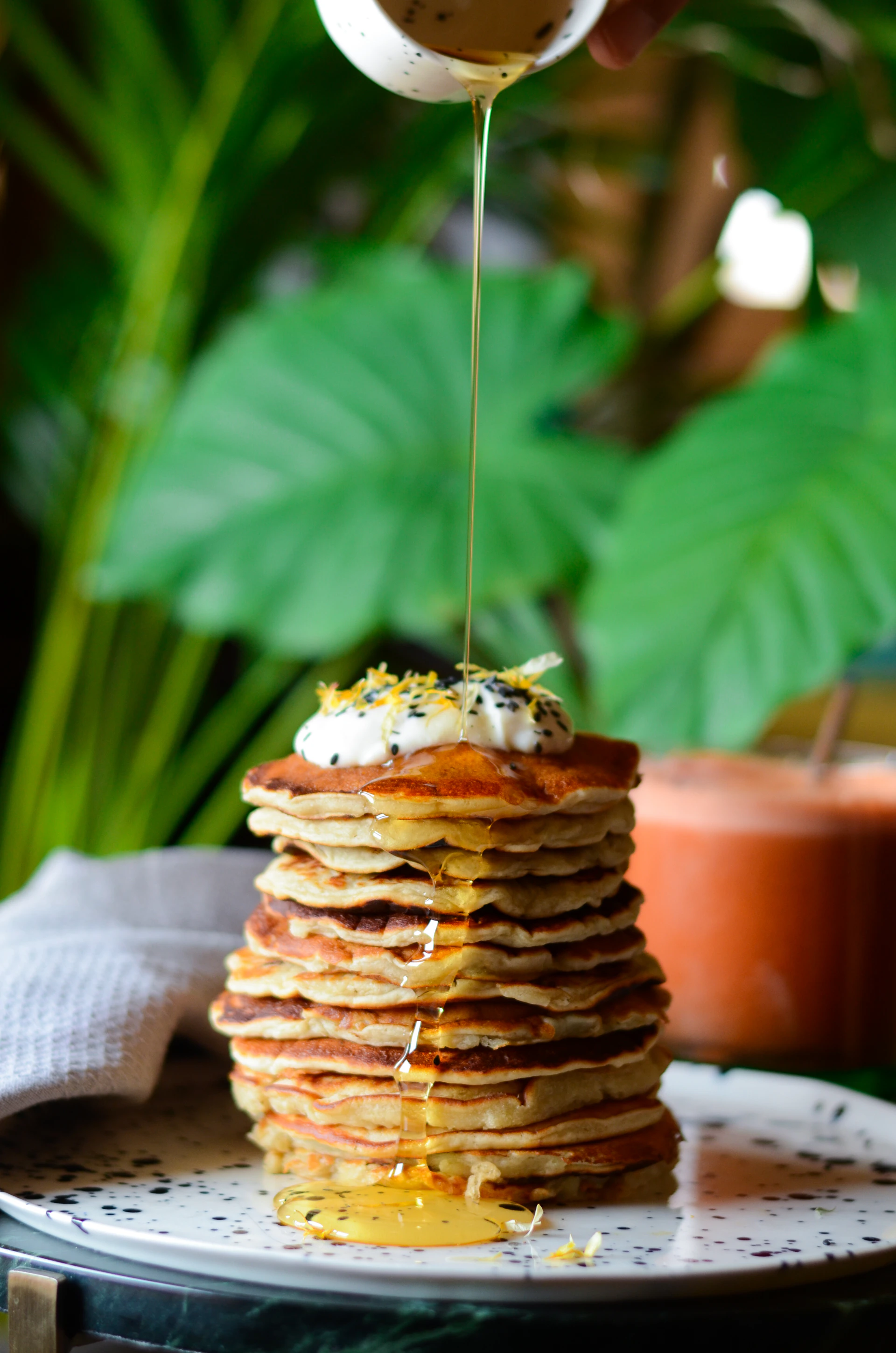 A tall mimosa glass sparkling in the morning light beside a stack of fluffy pancakes drizzled with syrup.