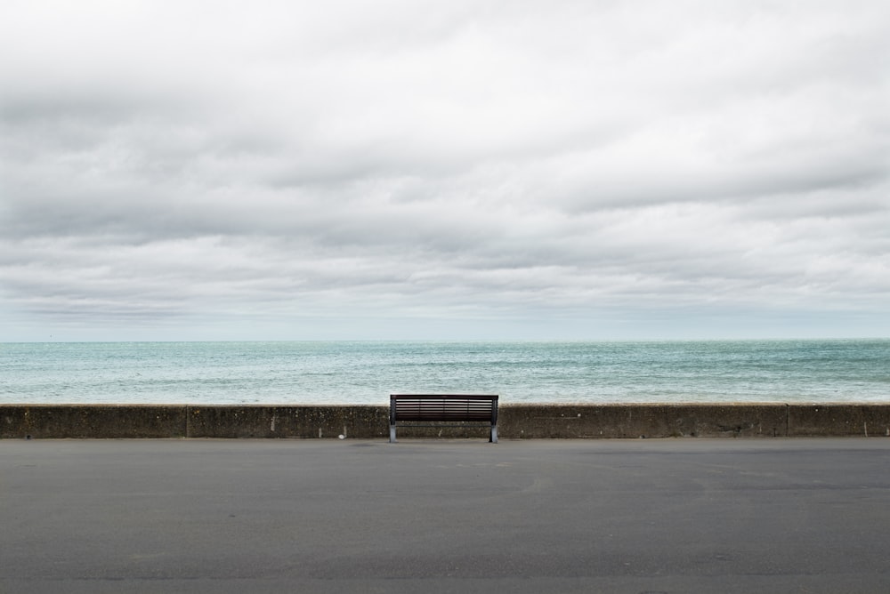 Banc en bois brun sur sol en béton gris près de la mer sous les nuages blancs pendant la journée