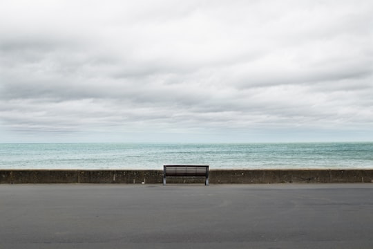 brown wooden bench on gray concrete floor near sea under white clouds during daytime in Cabourg France