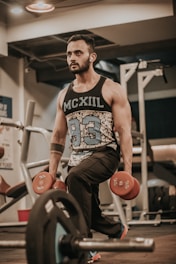 man in black and white tank top and brown shorts sitting on black and red exercise