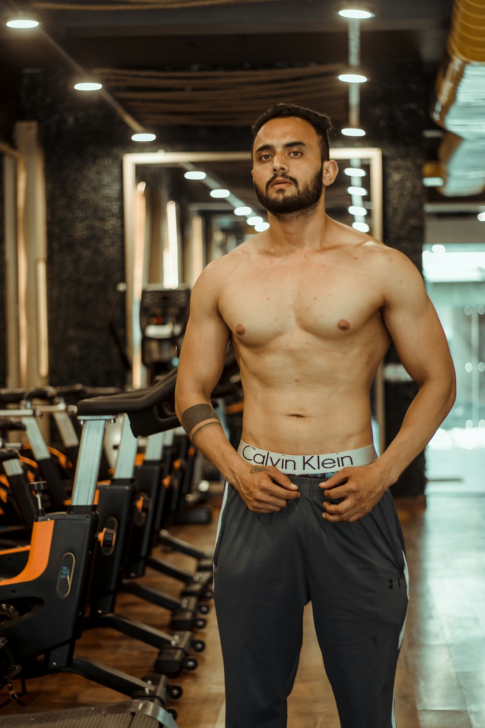 topless man in blue shorts standing near brown wooden bench