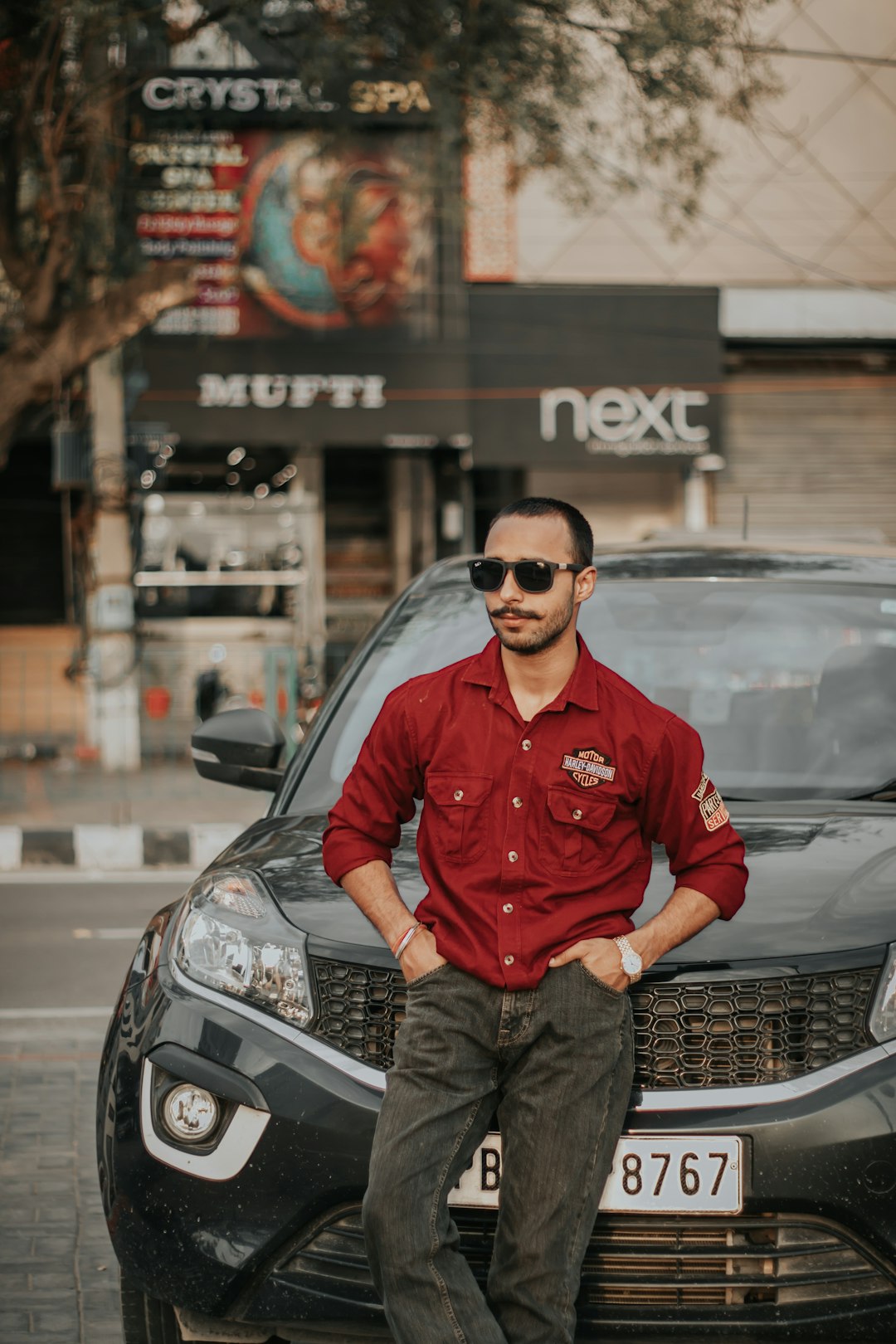 man in red long sleeve shirt and blue denim jeans sitting on black car