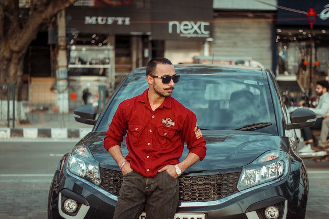 man in red dress shirt and black pants sitting on black mercedes benz car