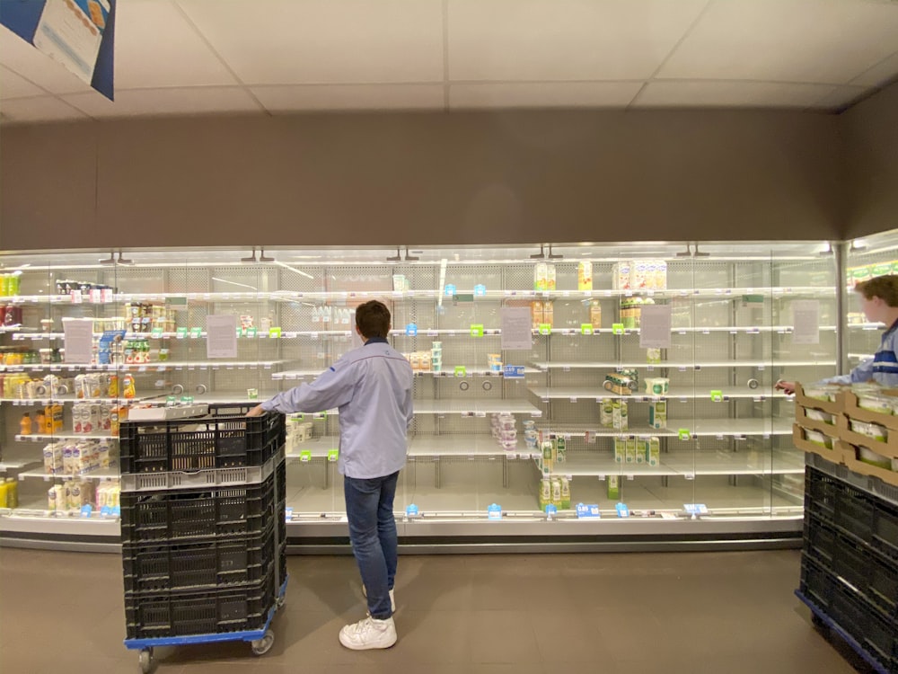 man in white dress shirt and blue denim jeans standing in front of white shelf