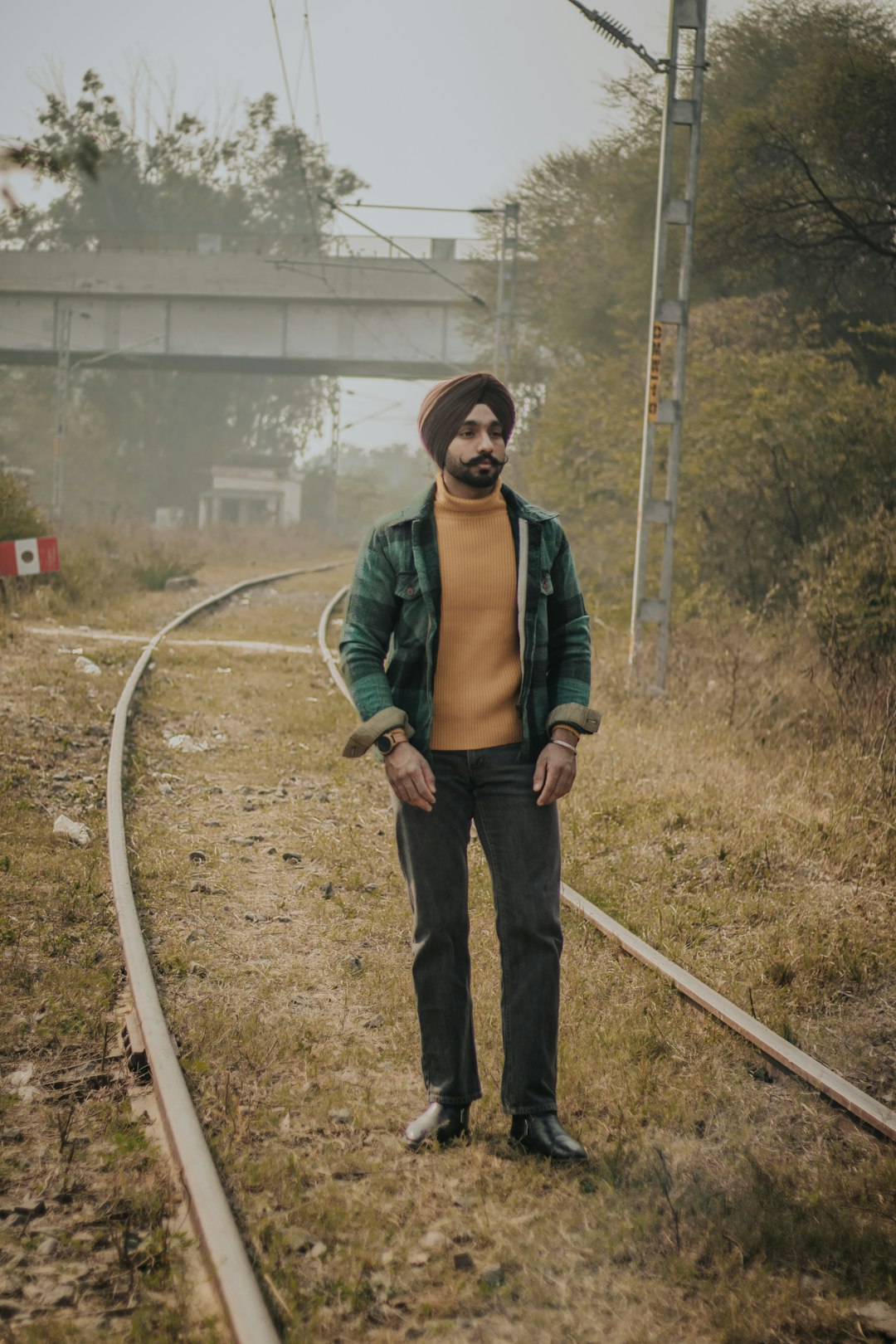 man in green jacket standing on train rail during daytime