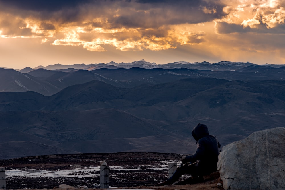 person sitting on rock near mountains during daytime