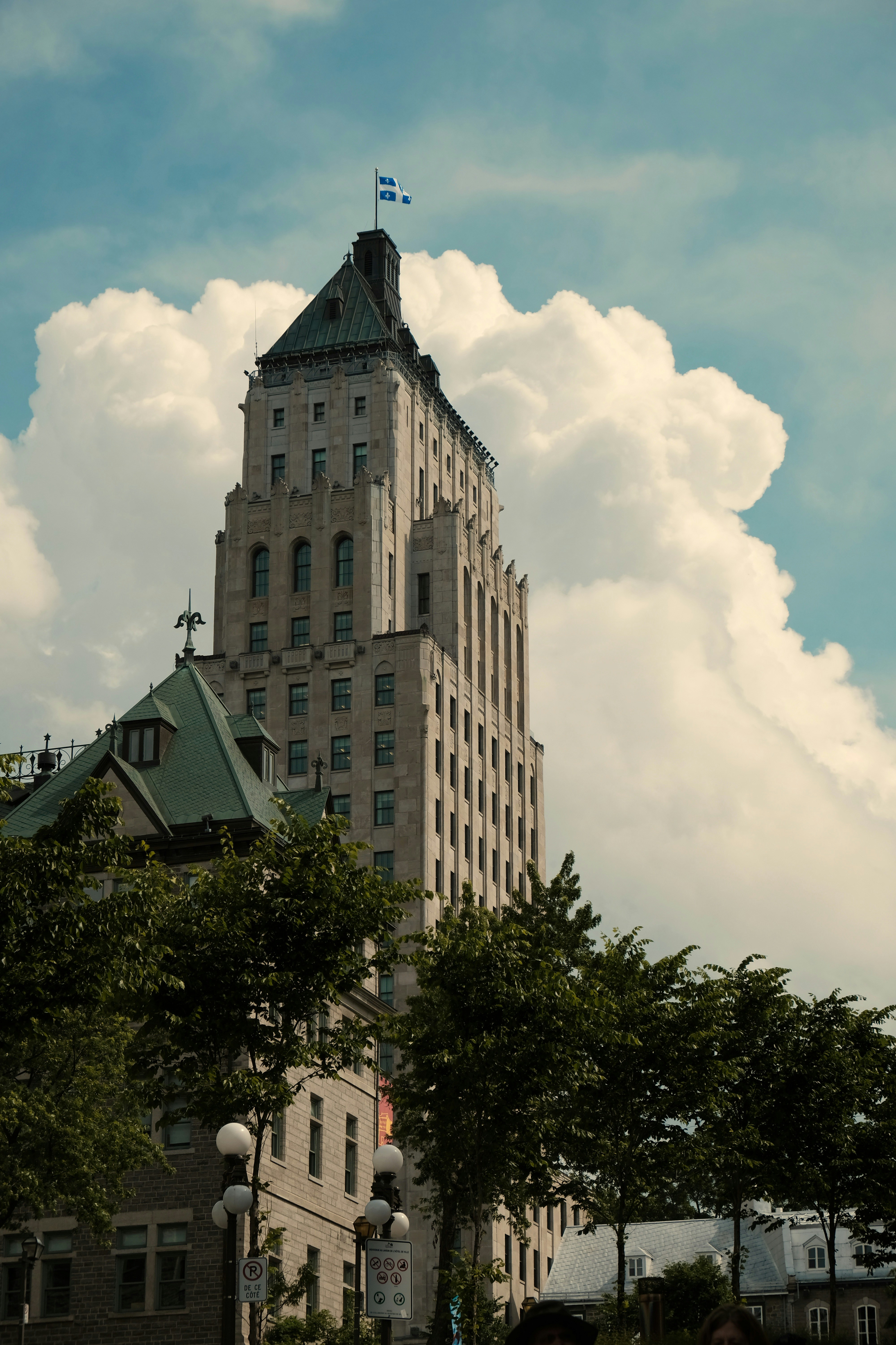 Grüne Bäume in der Nähe von braunem Betongebäude unter weißen Wolken und blauem Himmel tagsüber